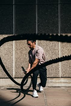 a man holding a bike tire while standing next to a building with a shadow on the ground