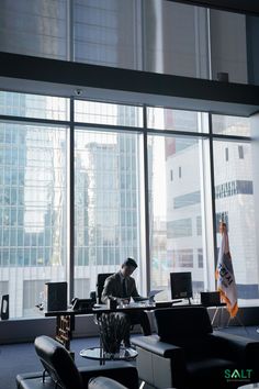 a man sitting at a desk in an office with large windows looking out onto the city