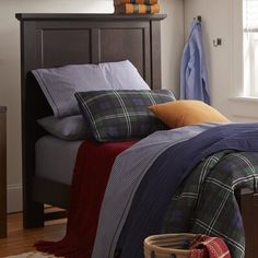 a bed with plaid sheets and pillows in a bedroom next to a basket on the floor