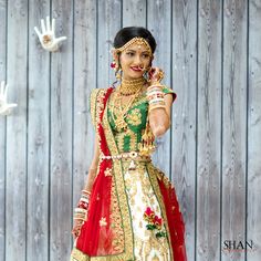 a woman in a red and green bridal outfit standing next to a wooden wall