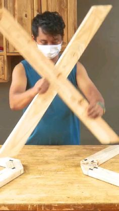 a man wearing a face mask is making wooden crosses