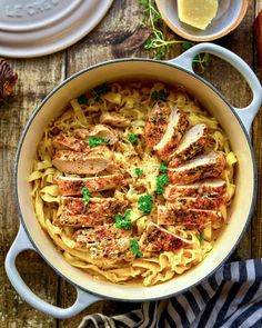 a pan filled with chicken and pasta on top of a wooden table next to other dishes