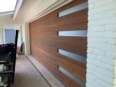 a wooden garage door in front of a white brick building with glass inserts on the side