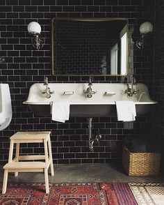 a black tiled bathroom with two sinks and a stool in front of the sink is a mirror