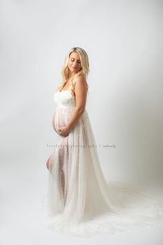 a pregnant woman in a white gown poses for a photo while holding her belly up