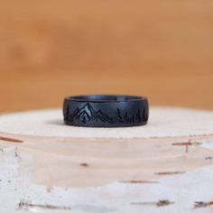 a black ring sitting on top of a piece of wood with mountains in the background