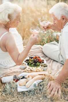 an older couple toasting wine glasses over a platter of food on the ground