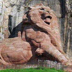 a large stone lion statue in front of a rock wall with grass growing around it