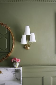 a bathroom with green walls and two lamps next to a sink in front of a mirror