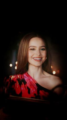 a woman in a red and black dress smiling at the camera with lights behind her