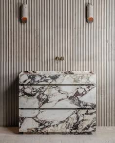 a white marble sink sitting in front of a wall mounted faucet with two lights on it