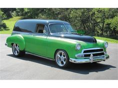 an old green and black station wagon parked in a parking lot with trees in the background