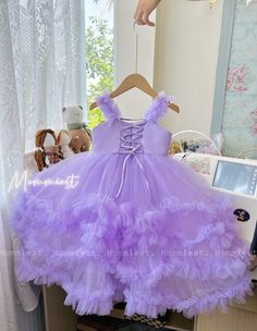 a purple dress hanging on a wooden hanger in front of a window with stuffed animals