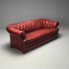 a red leather couch sitting on top of a white floor next to a gray wall