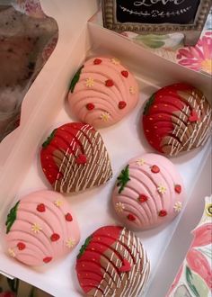 four decorated strawberry cookies in a box on a table with flowers and other items around them