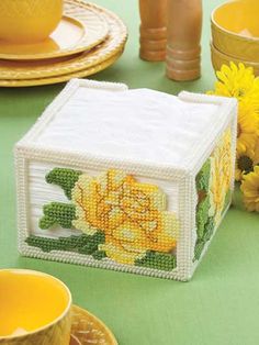 a cross stitch box sitting on top of a table next to yellow plates and cups