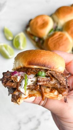 a hand holding a pulled pork sandwich with green onions and cilantro on the side