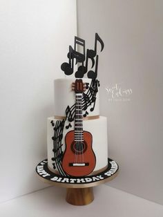 a cake decorated with musical notes and a red guitar on the bottom tier, sitting on top of a wooden stand