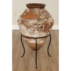 an old vase sitting on top of a metal stand with a wooden floor in the background