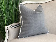 a gray pillow sitting on top of a couch next to a green plant