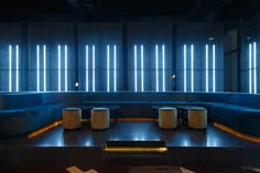 an empty room with blue couches and stools in front of neon lights on the walls