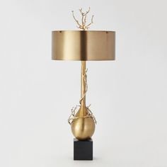 a gold lamp on a black stand with a beige shade over the base and branches sticking out of it