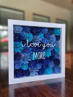 a white frame with blue paper flowers and the words i love you more