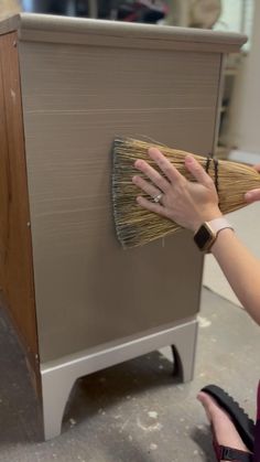 a woman is holding a broom over a cabinet