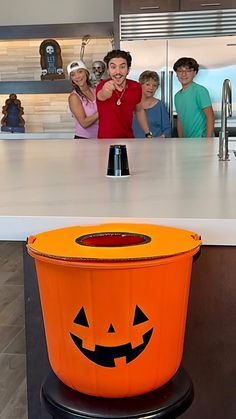 a group of people standing around an orange trash can with a jack - o'- lantern on it