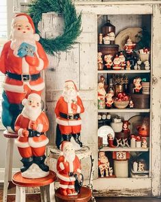 santa clause figurines sitting on stools in front of a shelf with christmas decorations