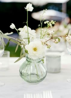 white flowers in a clear vase on a table with wine glasses and napkins around it