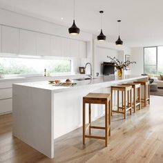 an open kitchen and living room area with white cabinets, counter tops, and bar stools