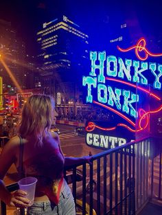 a woman standing on a balcony next to a neon sign that reads honky tonks center