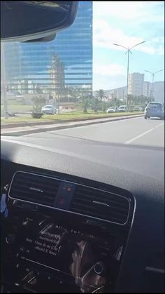 the dashboard of a car driving down a street with tall buildings in the background,