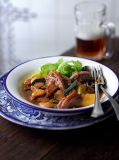 a blue and white plate topped with meat and veggies next to a glass of beer