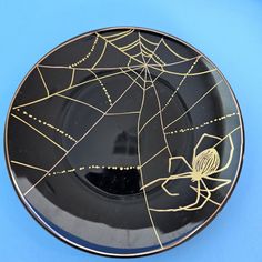 a black and gold plate with a spider web design on the front, against a blue background