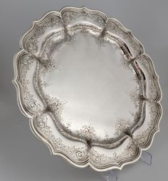 an antique silver plate with ornate designs on the rim and sides, set against a gray background