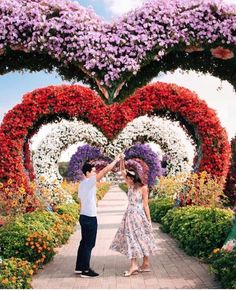 a man and woman standing in front of a heart shaped flower garden with lots of flowers