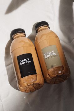 two bottles of coffee sitting on top of a white sheet covered bed next to each other