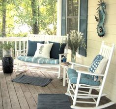 a porch with white rocking chairs and blue pillows on the front porch, next to trees