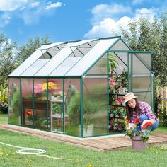 a woman kneeling down next to a green house with flowers in it and potted plants on the ground