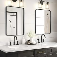 two sinks and mirrors in a bathroom with lights on the wall above them, along with a vase filled with flowers