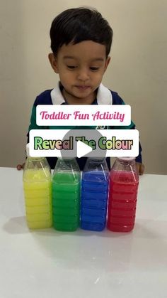 a young boy sitting at a table in front of four plastic containers filled with liquid