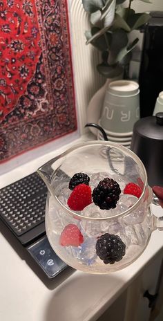 a glass bowl filled with berries on top of a white table next to a laptop