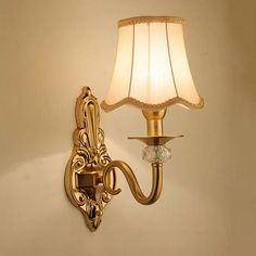 a gold wall light with a white shade on it's arm and lamp attached to the wall