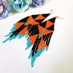 an orange and black beaded earrings on a white surface with flowers in the background