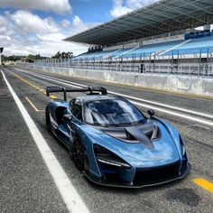 a blue sports car driving on the road in front of an empty race track with bleachers