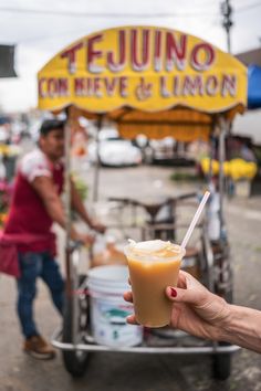 a person holding up a drink in front of a food cart with a man behind it