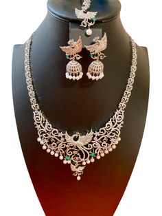 This elegant South Indian Haaram features a stunning Double Peacock Design adorned with CZ American Diamonds. It is perfect for special occasions such as marriage ceremonies, parties, or as a gift for someone special. Complete your Indian outfit, such as a silk saree or gown, with this beautiful piece. This jewellery set includes a necklace, matching earrings and a maang tika. Jewellery Care- Keep the jewellery dry, avoid contact with perfumes and water. Festive Peacock Design Bridal Necklace For Reception, Elegant Bridal Necklace With Peacock Design For Diwali, Silver Peacock Design Bridal Necklace, Silver Bridal Necklace With Peacock Design For Festivities, Silver Bridal Necklace With Peacock Design, Silver Bridal Necklace With Peacock Design For Wedding, Festive Silver Bridal Necklace With Peacock Design, Festive Silver Peacock Bridal Necklace, Elegant Green Bridal Necklace With Peacock Design