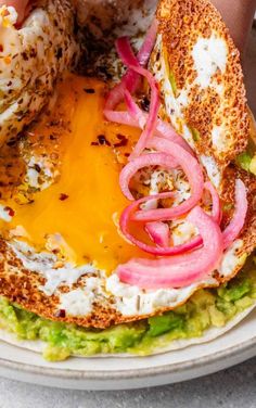 someone is holding up a sandwich with onions and cheese on it in front of the camera